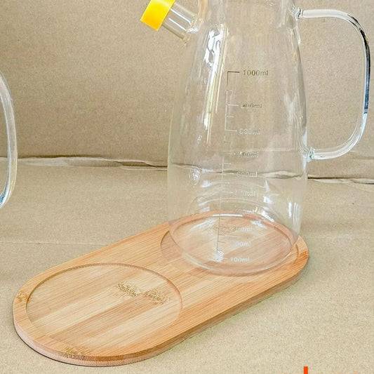 Erkugo'dan Bambu Yağdanlık Altlığı 2 Bölmeli üzerinde ölçü işaretli şeffaf cam sürahi bulunmaktadır. Çok amaçlı kullanım için tasarlanmış olup, kulplu, sarı uçlu ağızlıdır ve nötr bej bir yüzey üzerinde durmaktadır.